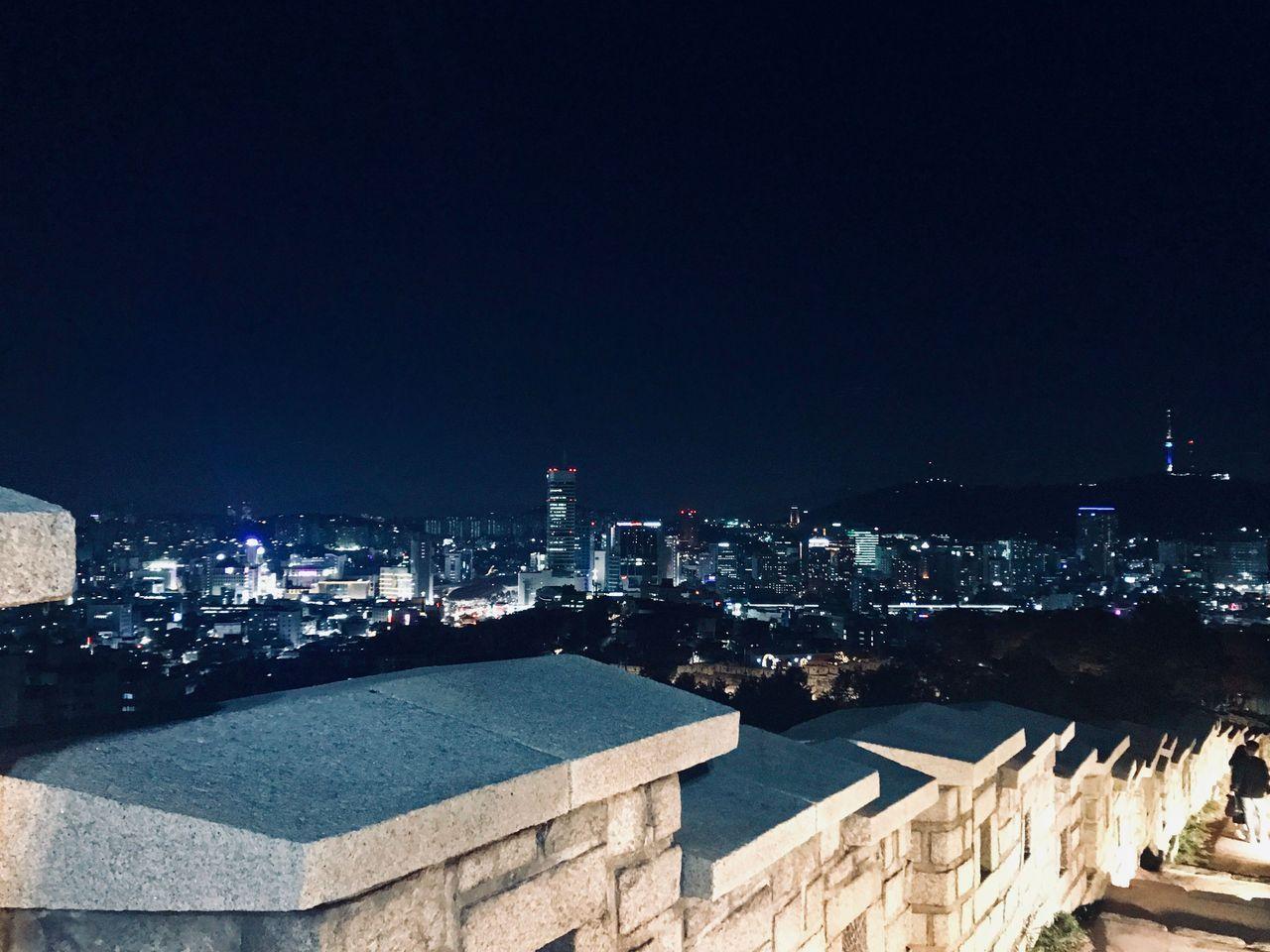 首尔骆山公园的石墙和都市夜景，明亮的灯光下。